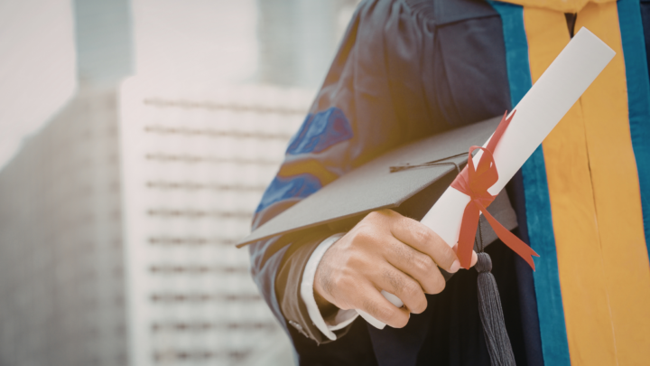 Gros plan sur une personne en tenue de diplômé et tenant un diplôme entouré d'un ruban dans sa main