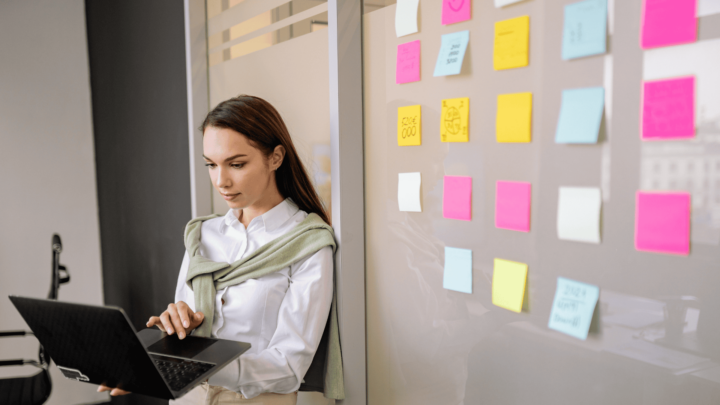 Femme debout travaillant sur son ordinateur avec à sa gauche, des post-its colorés sur un mur