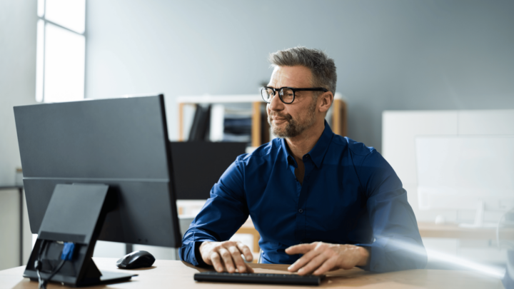Homme en chemise et à lunettes travaillant devant son ordinateur